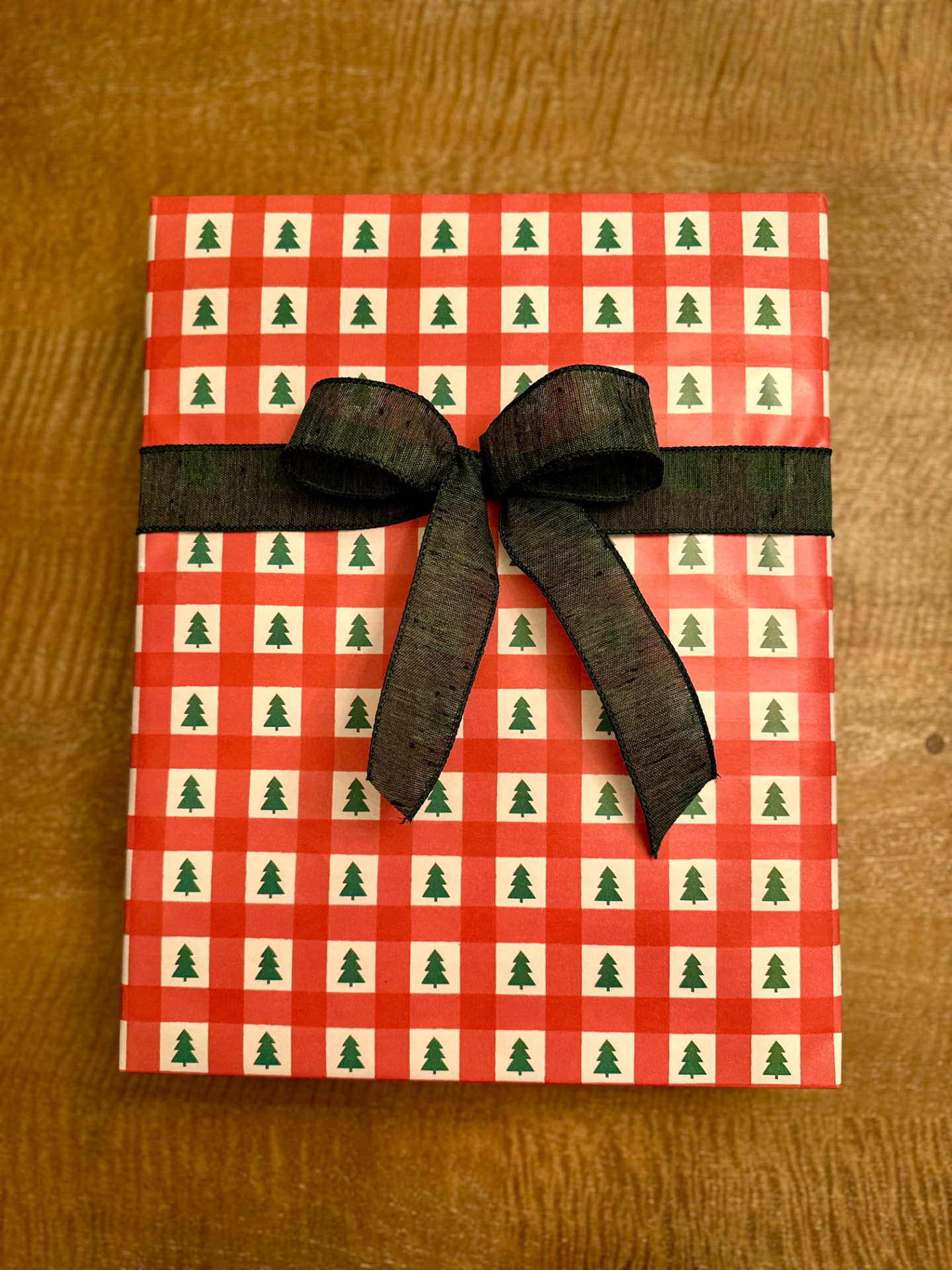 Close-up of a gift wrapped in red plaid paper with green trees and a dark green ribbon bow